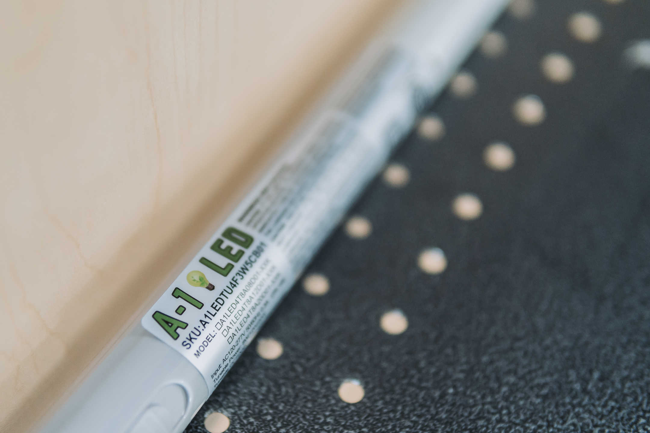 A white LED tube light labeled A-1 LED is resting on a dark surface with evenly spaced holes and a light wooden background.